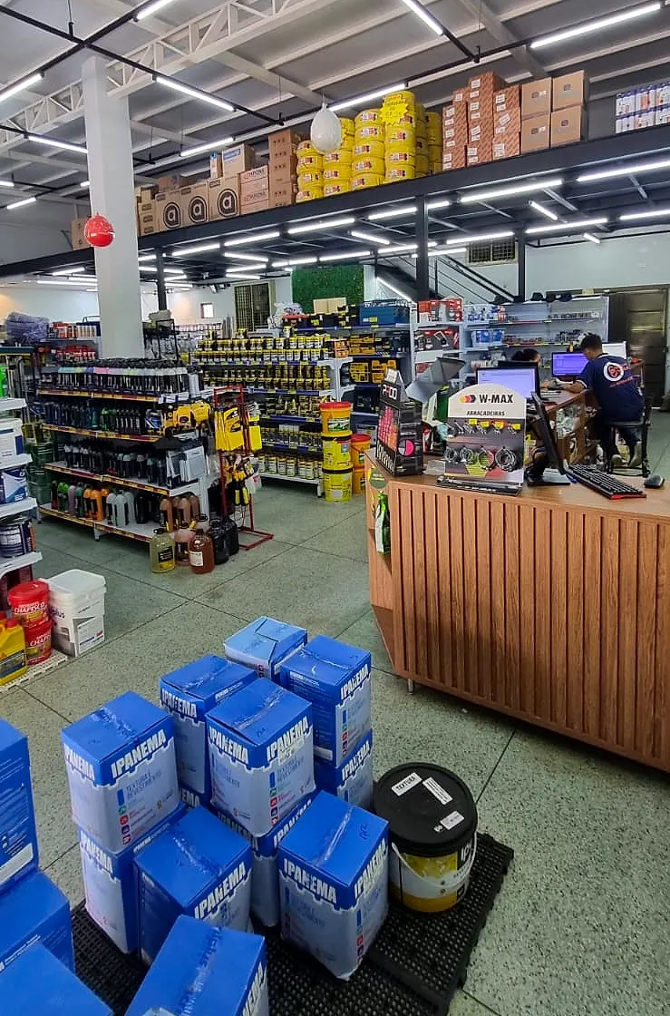 Balcão de atendimento da Comercial Central com atendente e corredores de ferragens ao fundo